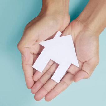 Two hands holding paper cut out house